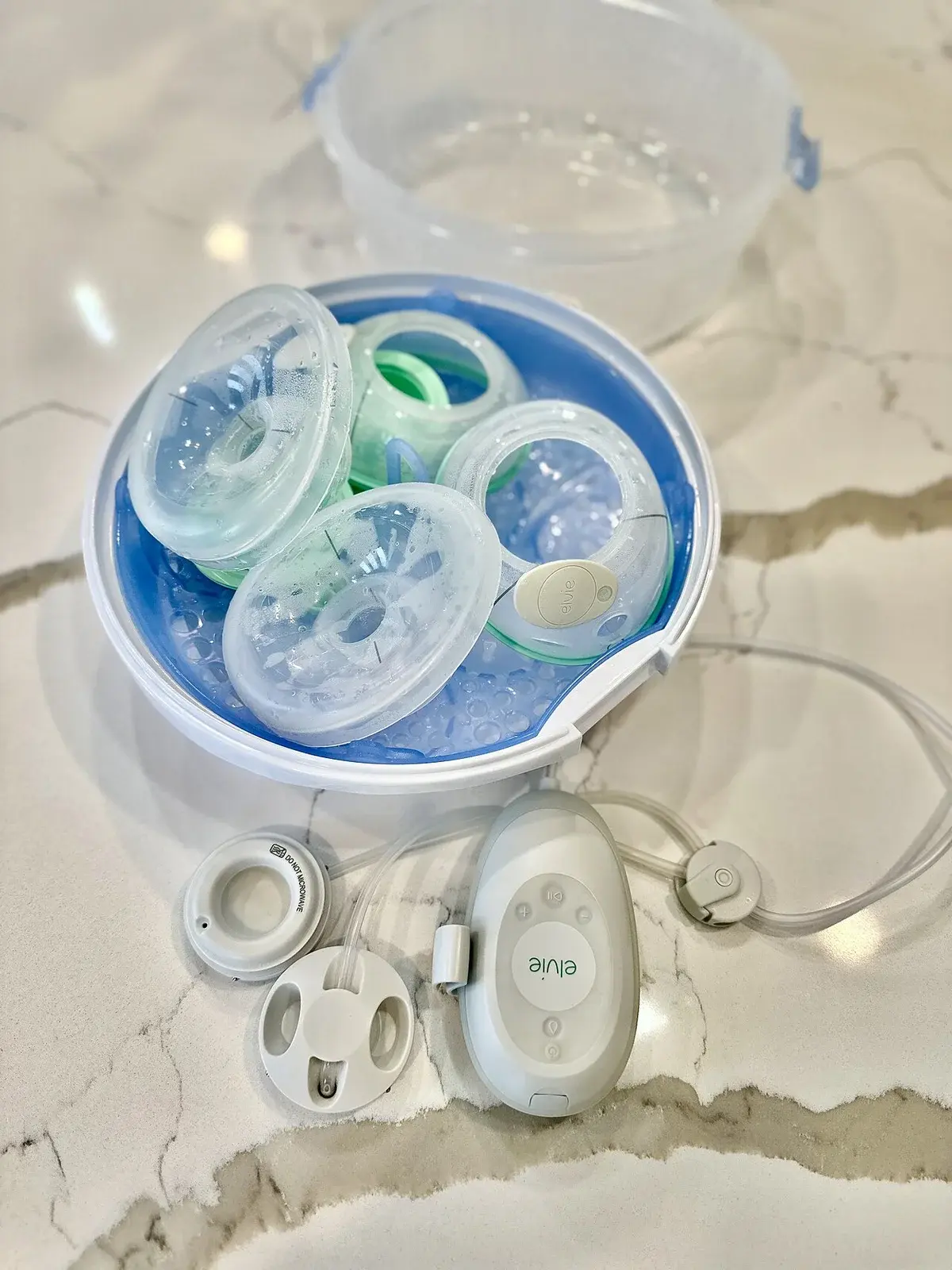 Hands-free breast pump parts in a microwave sterilizer on a countertop.
