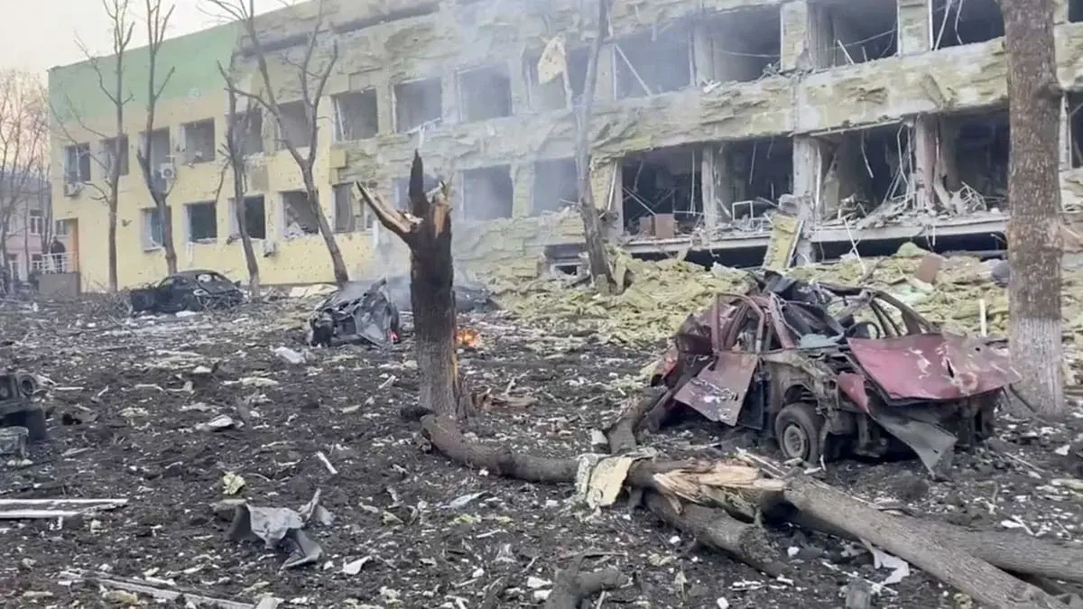 Destroyed hospital building with debris and burned-out cars in Mariupol.