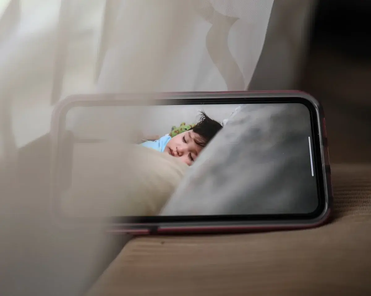 A smartphone shows a sleeping child on a baby monitor feed.