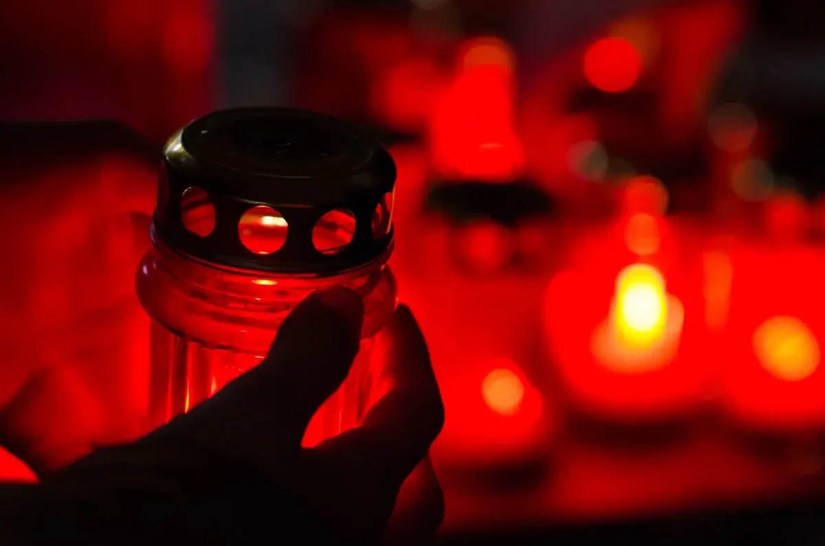 A silhouetted hand holding a red memorial candle at night.